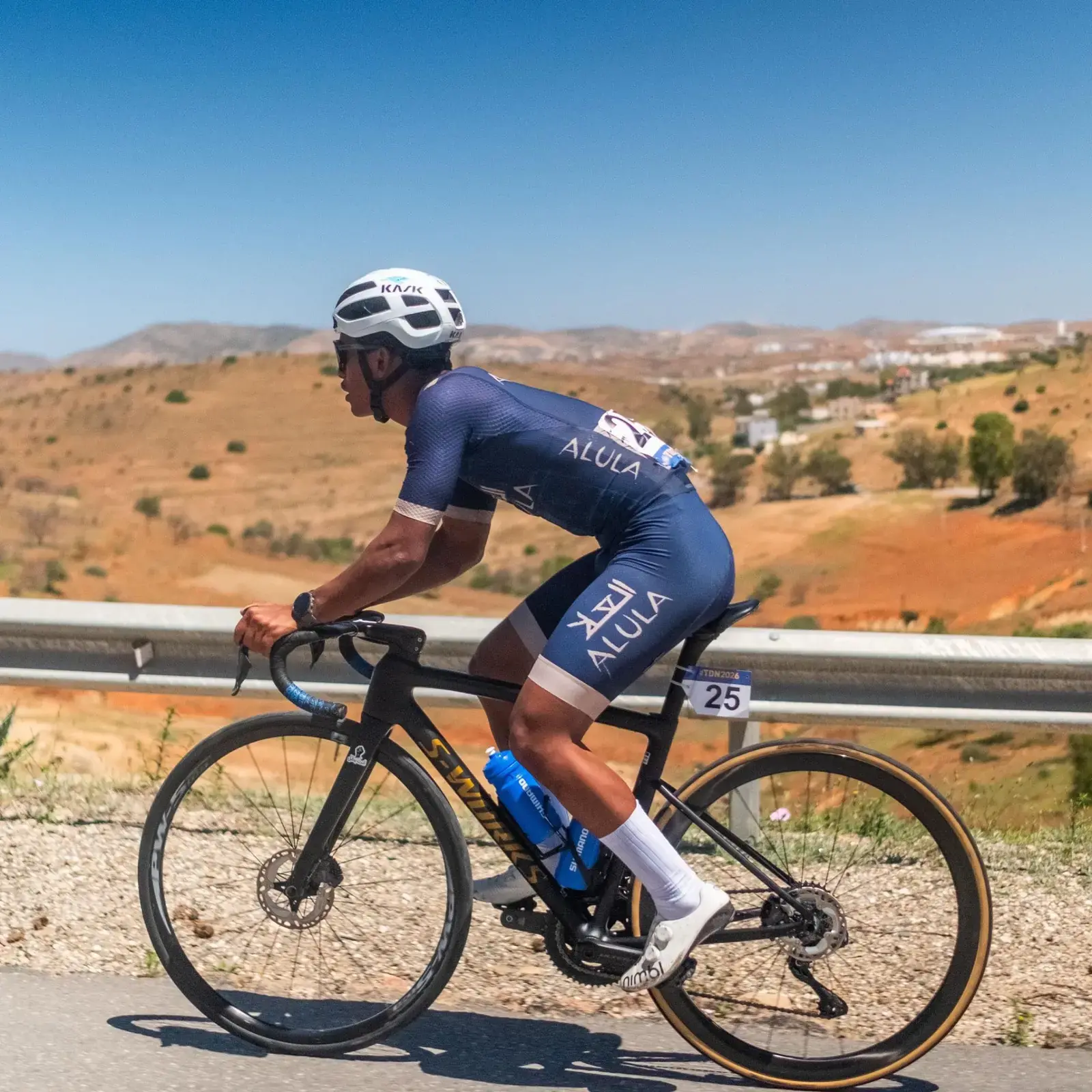 AlUla team cyclist riding through a dry hillside landscape