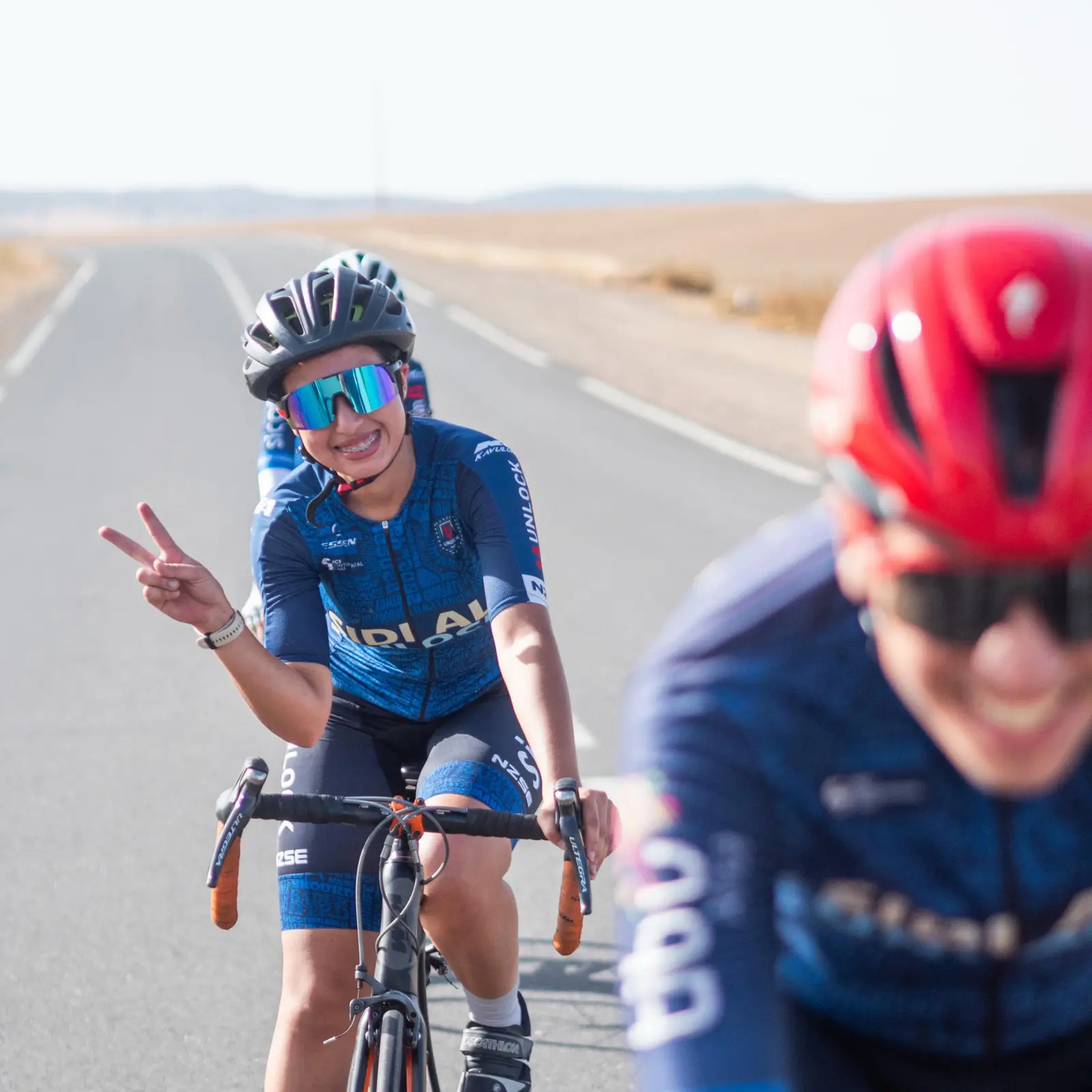 Female Sidi Ali cyclist smiling and giving a peace sign on an open road