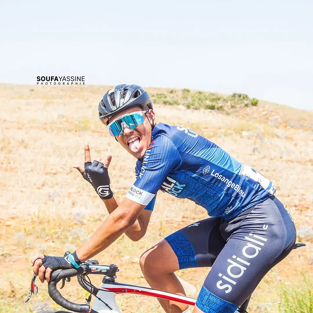 Sidi Ali cyclist smiling and making a hand gesture while riding through a dry landscape